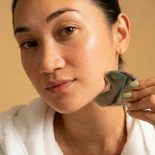 Skin-Nomad stainless steel gua sha, a contoured facial massage tool, photographed on a neutral surface